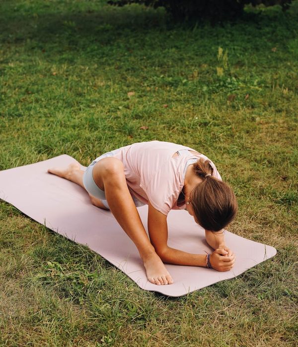 Person stretching gently on a yoga mat outdoors.